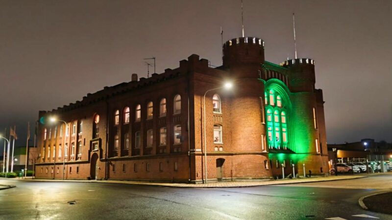 Röd tegelbyggnad med grönt ljus på fasaden under kvällstid