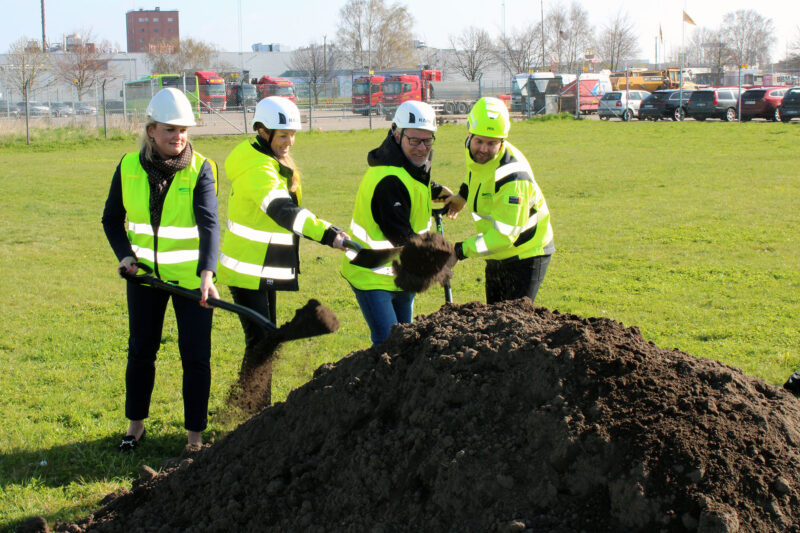 Fyra personer i varselkläder skyfflar jord vid en stor jordhög